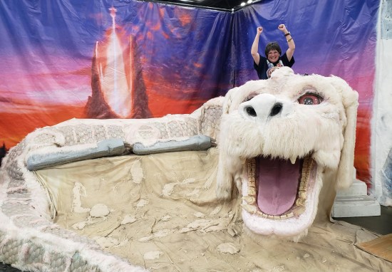 Anne atop the fuzzy Falkor replica, her arms raised like it's a roller coaster.