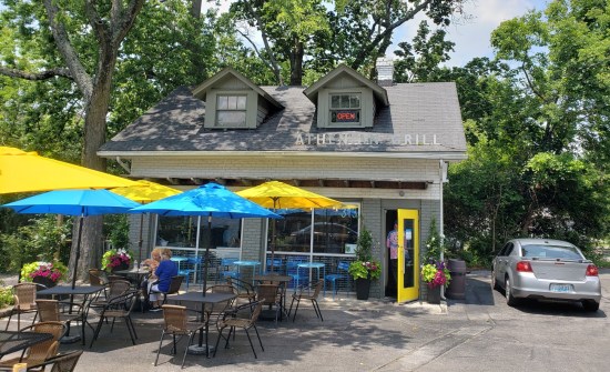Greek restaurant in a small, two-story house with outdoor patio tables, chairs and umbrellas.