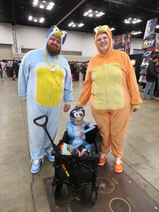 cosplay: Bluey and Bingo parents of a tiny Bluey in a red wagon playing video games.