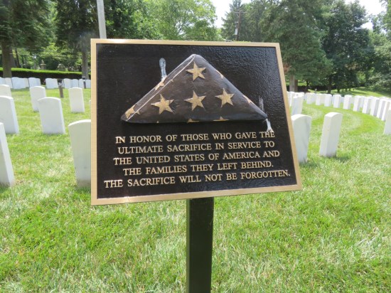 A folded flag mounted on a plaque on a stand in a cemetery.  The text: "In honor of those who gave the ultimate sacrifice in service to the United States of America and the families they left behind. The sacrifice will not be forgotten."