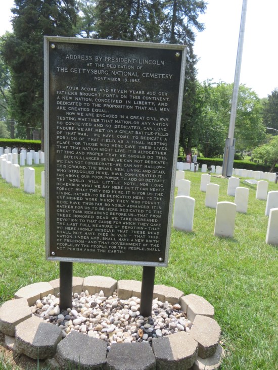Five-foot plaque standing upright, encircled by white rocks, bearing the full text of the Gettysburg Address.