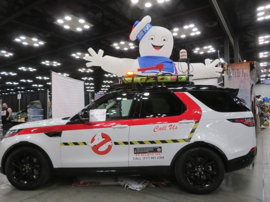 A white SUV with Ghostbusters trimmings. Behind it is an inflatable Sta-Puf Marshmallow Man.