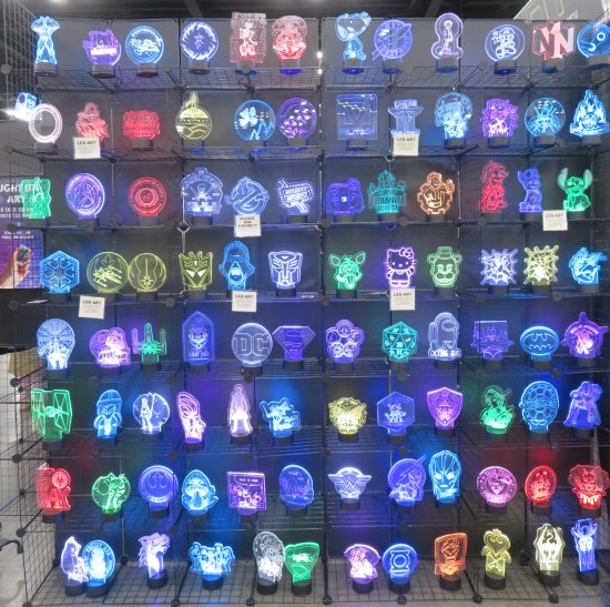 Dozens of light-up glass replicas of assorted logos and characters shelved on an exhibit hall wall.