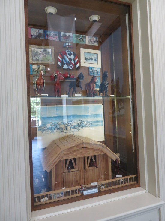 Glass wall case with horse racing souvenirs and merch not for sale.