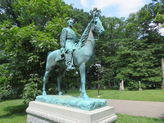 Turquoise confederate general statue on horse in wooded cemetery.