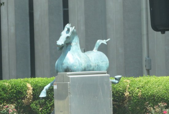 Blue running horse statue a bit far away, partially obscured by a gray electrical box.