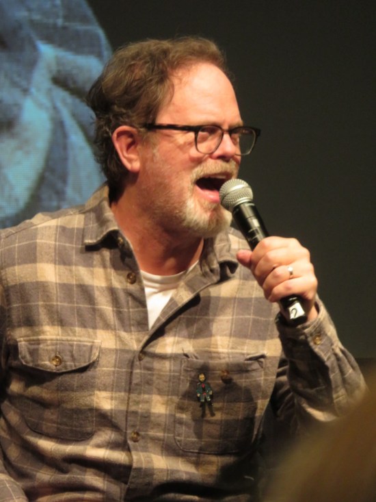 Rainn Wilson yelling into a mic onstage.