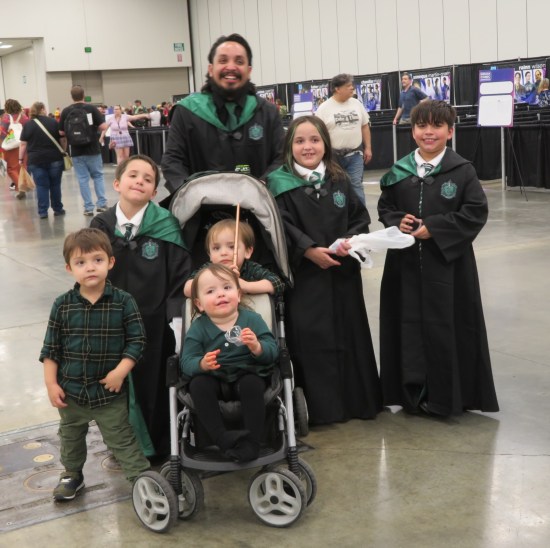 cosplay: a dad and three kids in Slytherin robes, two more kids in flannel shirts the same shade of green, and a baby a stroller with the same-colored top.