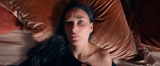 Demi Moore lying askew in bed, all encased in red, head at a weird angle and with a faraway look of terror.