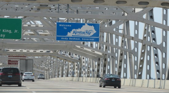 Driving inside an interstate bridge made entirely of white girders. Blue sign welcomes us to Kentucky. Traffic is light for now.