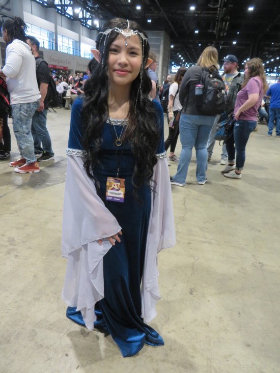 Young Arwen cosplayer in blue and white dress and gold crown.