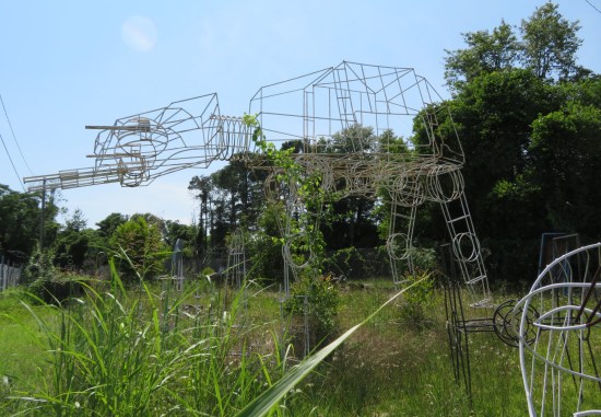 AT-AT sculpture 16 feet tall made of white wires, standing outside in an overgrown yard.