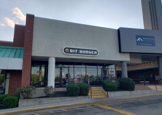 Bit Burger storefront next to a gray church. The sign is in Nintendo font and has a tiny video game burger on it.