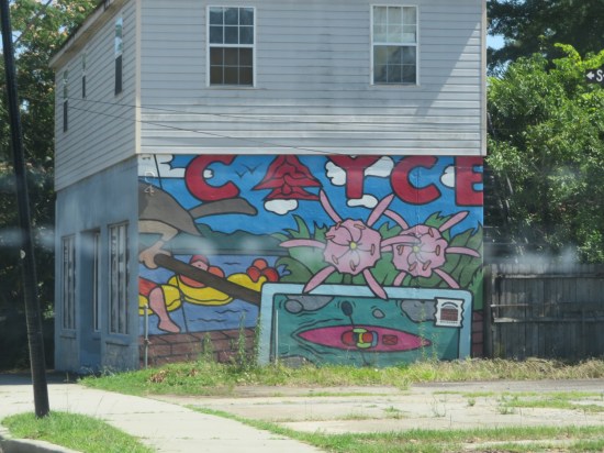 Mural that says CAYCE in big red letters above an image of a river with innertubers, one kayaker, and giant pink flowers.