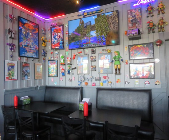 Black restaurant booths with gray walls, covered with toys and art from video games and robot cartoons.