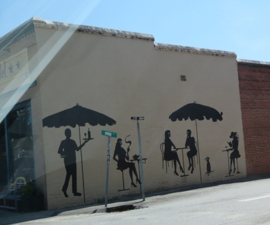 silhouettes of outdoor restaurant customers and patio furniture, painted on the side of a cafe.