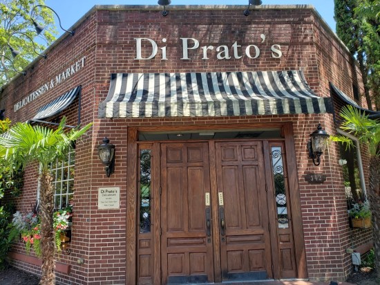 Brown exterior of DiPrato's Deli and Market. Brick walls, wooden double doors, black-and-white striped awning.