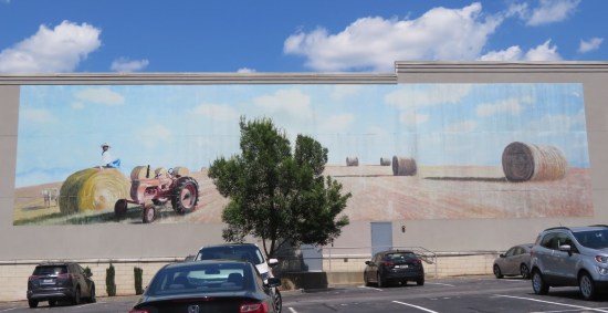 Mural of a stretch of farmland with a tractor and several large hay rolls. A tree blocks the middle of the mural.