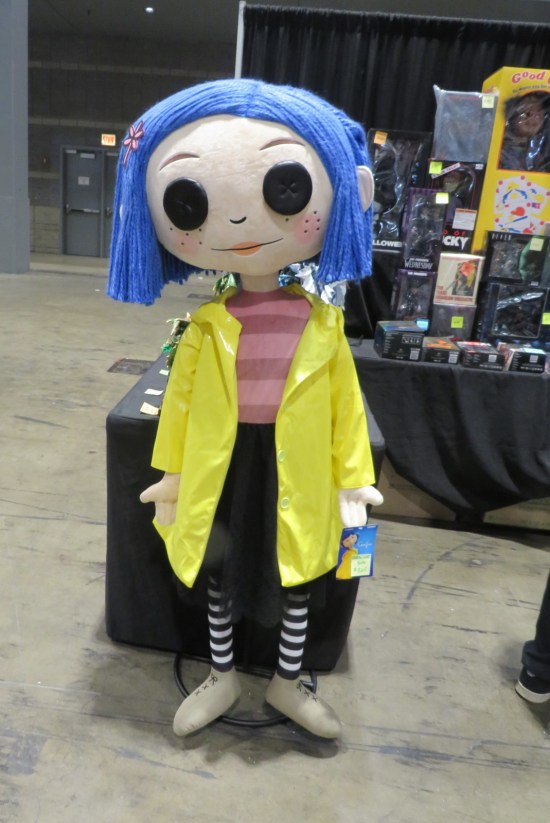 giant Coraline doll standing outside a booth draped in black.