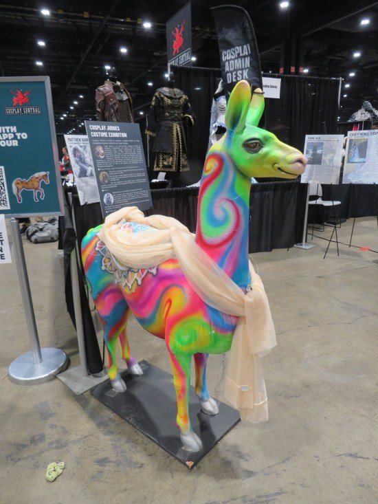Llama statue painted in tie-dyed colors, standing next to a booth labeled Cosplay Admin Desk.