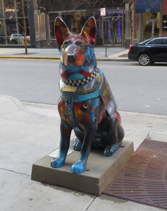 Dog statue with "Paws Chicago" tag, checkered collar painted on, and "Hotel EMC2" written on its chest.