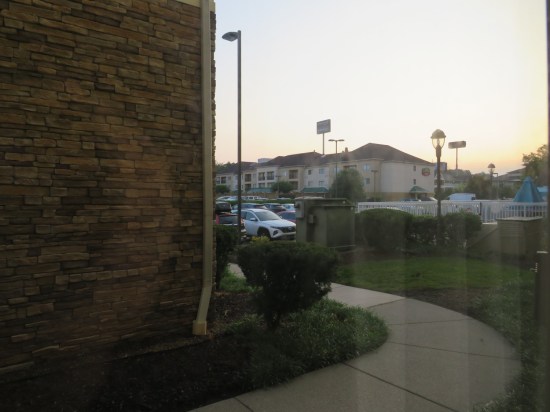 Outside our room: grass, shrubs, pool furniture, white fence, parking lot, another chain hotel.