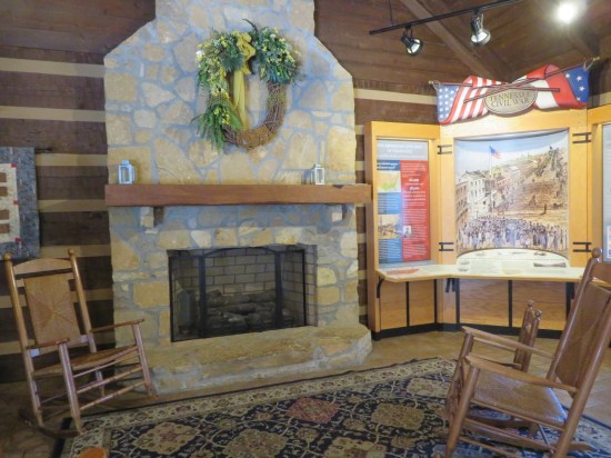 A fireplace and two wooden rocking chairs share a room with a museum display about Tennessee's role in the Civil War.