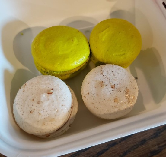 Four macarons in two flavors in a single Styrofoam takeout box.