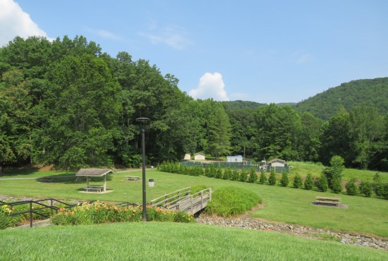 Several well-trimmed grassy acres of sloping hills with trees, a creek with rock-covered banks, a wooden bridge over same, some kind of small electrical station or other such utility, and some forested Appalachians out to the horizon.
