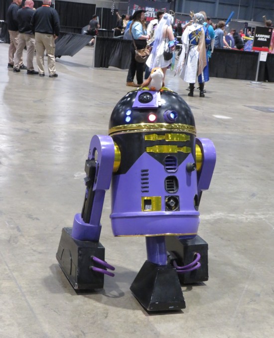 Purple astromech flitting about a concrete floor.