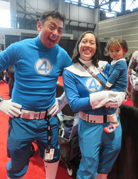 Cosplayers as Mr. Fantastic and the Invisible Woman, plus a baby also in a Fantastic Four onesie