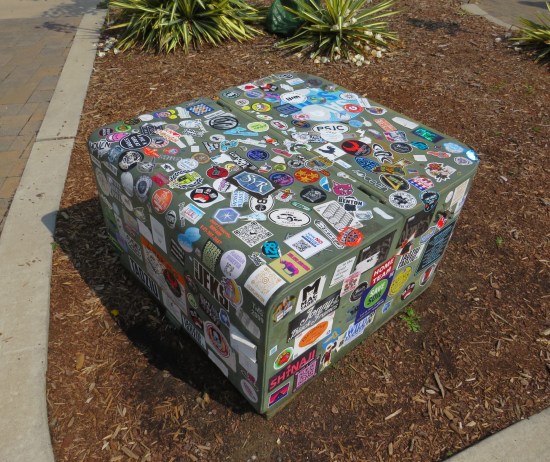 Squat gray sticker-covered electrical box surrounded by mulch.