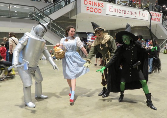 Four cosplayers as the Tin Man, Dorothy, the Scarecrow and the Wicked Witch of the West. Everyone's pointing at Dorothy's ruby slippers.