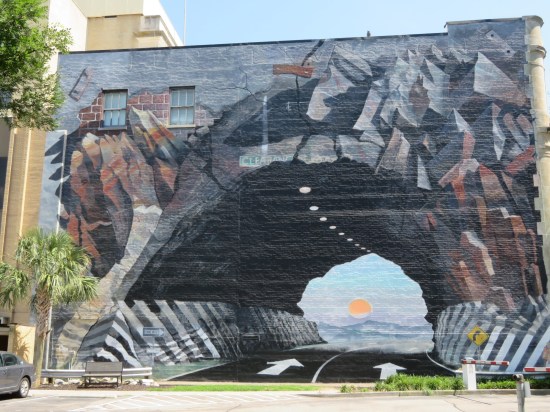 Large painting of a mountain tunnel, which covers an entire side of a building.