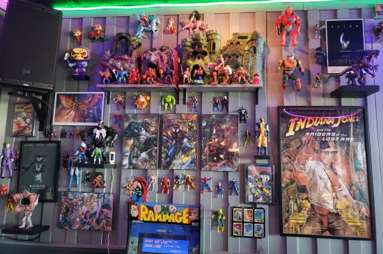 Restaurant wall covered in old action figures, Transformers, superhero art and a poster for "Indiana Jones and the Raiders of the Lost Ark".