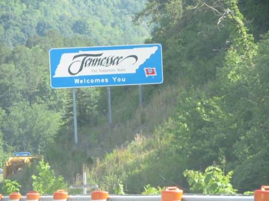 Welcome to Tennessee interstate sign in the middle of forested mountains. Roadside is lined with orange construction barrels.