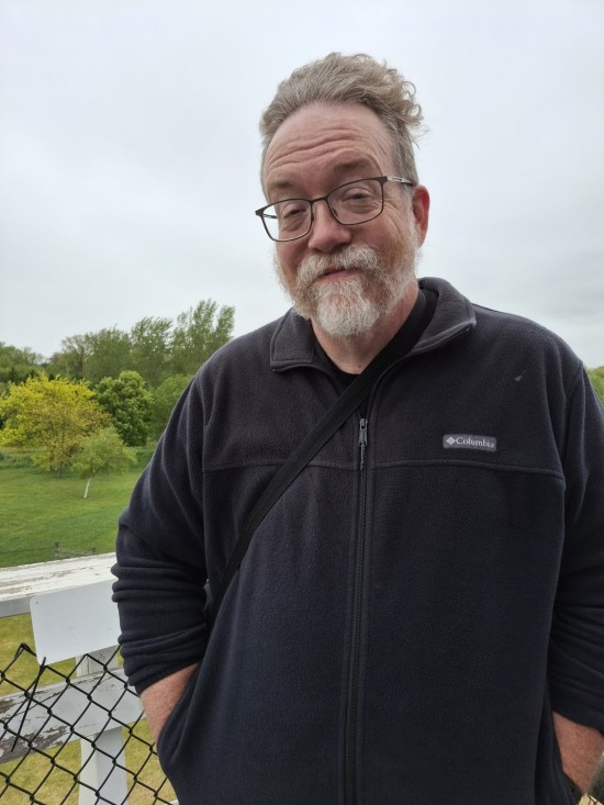 Me with jacket and gray beard, trying to smile while standing in cold winds on a platform four stories up.