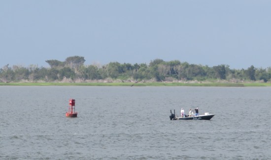 in harbor are a red buoy and a small fishing boat called HUK with three passengers.