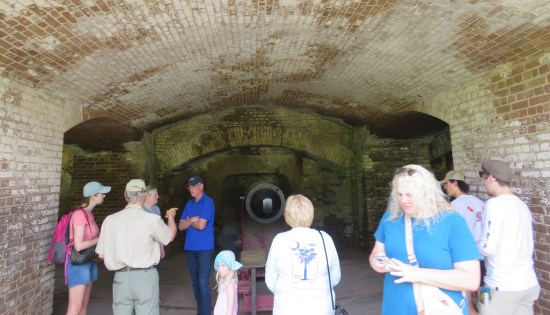 Deep cannon alcove with brick walls and ceiling. Tourists mill about, at least one playing on their phone.