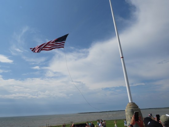 33-star US flag being raised up a pole. Bright cloudy skies behind it.