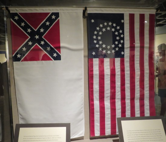 Two flags named in caption, hanging vertically in museum glass.