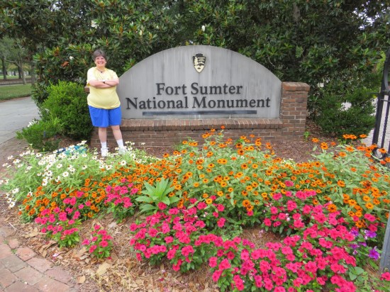 Anne smiling in front of a Fort Sumter National Monument sign, which has a pretty garden in front of it.