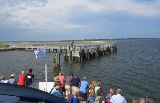 large boat with milling passengers approaches island pier.