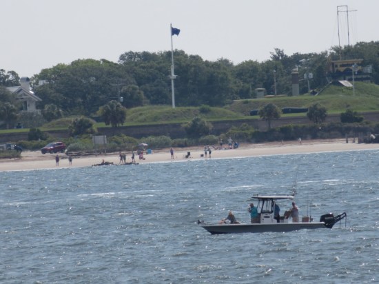 Faraway beach with a handful of folks. In the harbor is a slightly larger boat with a cabin and four passengers.
