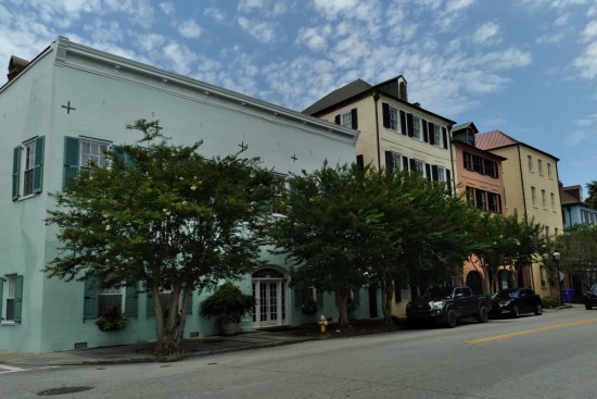 Trees obscure Rainbow Row houses that are aquamarine, old manila, peach, and newer manila.
