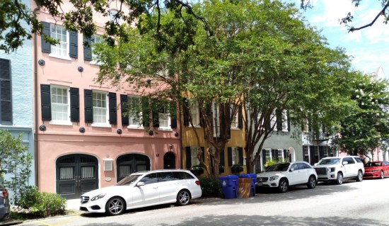 At least four Rainbow Row three-story houses in pink, orange, greenish-blue and white. Trees on the sidewalk obscure them.