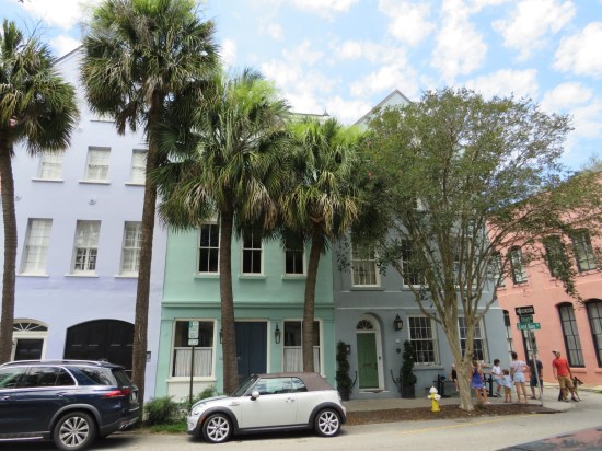 Rainbow Row houses in purple, teal, light blue and pinkish-orange with palmettos and other trees out front.