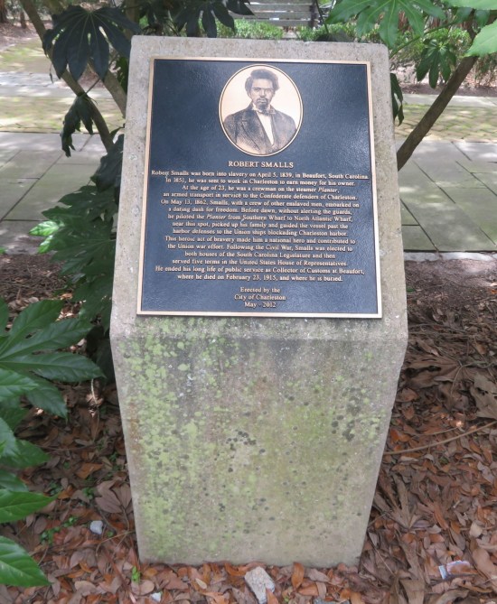 Plaque on a small stone pedestal on the edge of a city park.