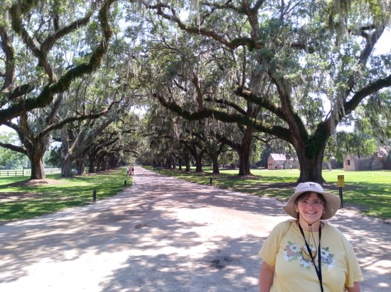 Anne in front of a road that's lined on either side by extremely tall oak trees.