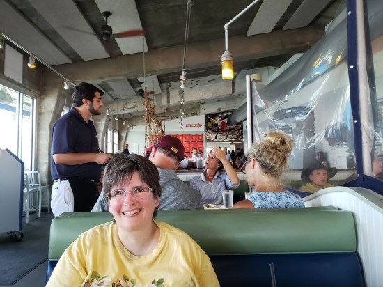 Anne sitting across from me in a green booth. Behind her, a family of four orders from their waiter. To her left and my right, a plastic sheet separates us from other tables.